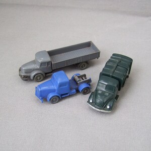 以下が含まれることがあります： グレー、ブルー、グリーンの3台の玩具トラック。グレーのトラックは荷台付き、ブルーのトラックはキャビンとトレーラー付き、グリーンのトラックは箱型のボディ付きです。