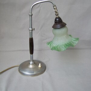 Könnte beinhalten: Eine vintage Schreibtischlampe aus Chrom und Holz mit einem grünen Glasschirm. Die Lampe hat einen flexiblen Arm und einen runden Sockel.