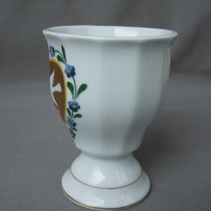 K&ouml;nnte beinhalten: Ein wei&szlig;er Porzellan-Eierbecher mit goldfarbenem Rand und einem Blumendesign mit blauen Blumen und braunen V&ouml;geln.