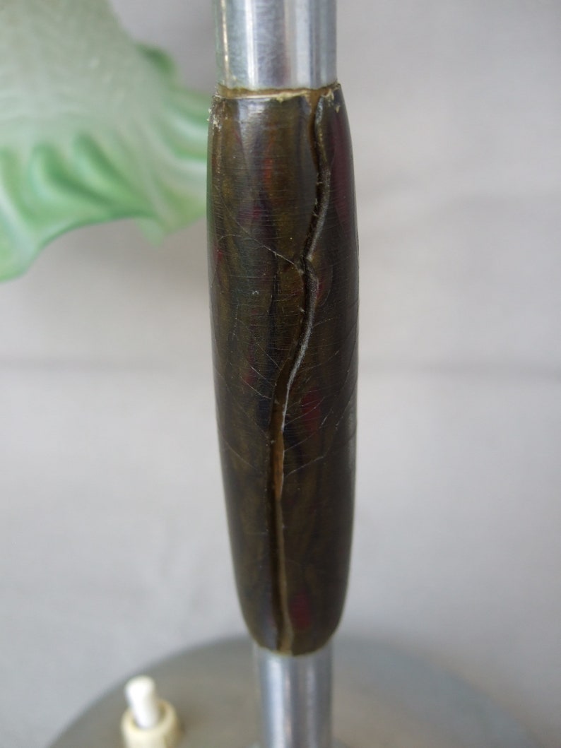Op de afbeelding: Een lamponderdeel met een cilindervormige, donkerbruine handgreep met een gemarmerde textuur en een verticale barst in het midden, gemonteerd op een zilverkleurige metalen stang boven een ronde voet met een kleine witte drukknopschakelaar.
