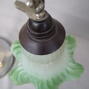 Op de afbeelding: Een lampenkap van matglas met een lichtgroene, gegolfde rand en een geribbelde textuur. De kap is bevestigd aan een donkerbruine ronde fitting, die verbonden is met een metalen scharnierarm met een zichtbare vleugelmoer aan de bovenzijde.