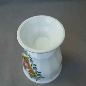 K&ouml;nnte beinhalten: Ein wei&szlig;er Keramik-Eierbecher mit floralem Design. Das Design zeigt rosa und blaue Blumen um einen goldenen Buchstaben "A".
