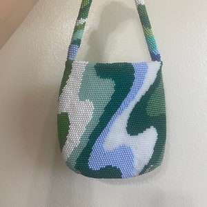 May include: A small, green, blue, and white beaded handbag with a curved shape and a beaded strap.