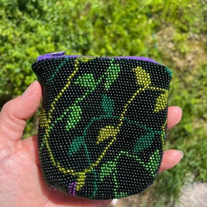 Peut inclure: Une petite bourse à monnaie noire en perles avec une fermeture à glissière. La bourse est décorée d'un motif floral dans des tons de vert et de jaune.