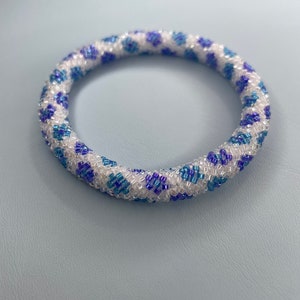 Op de afbeelding: Een witte kralen armband met een blauw en paars geometrisch patroon.