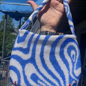 May include: A small blue and white beaded handbag with a wavy pattern. The bag has a top handle and is made of small, round beads.