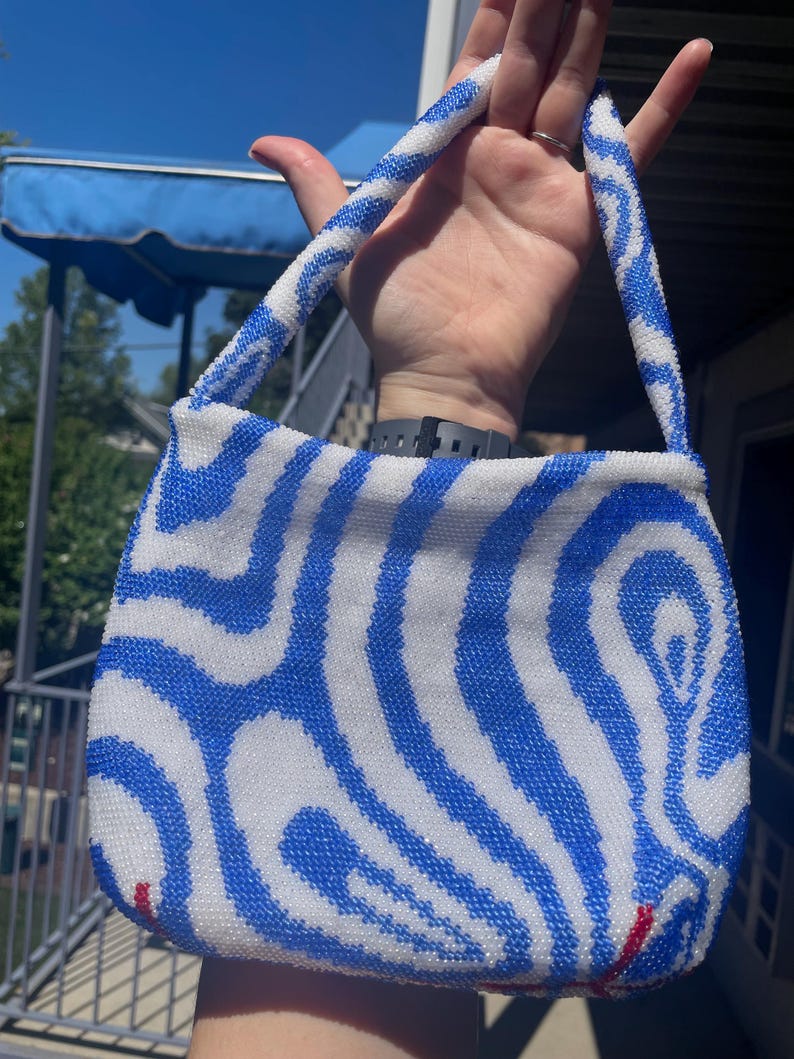 May include: A small blue and white beaded handbag with a wavy pattern. The bag has a top handle and is made of small, round beads.