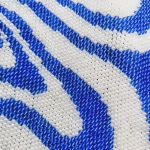 May include: Close-up of a beaded fabric with a wavy pattern in white and blue.