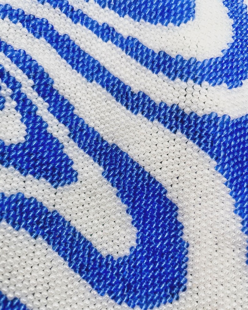 May include: Close-up of a beaded fabric with a wavy pattern in white and blue.
