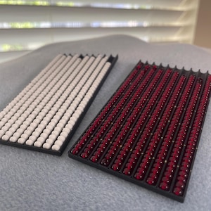 May include: Two rectangular trays filled with small, round beads. One tray has white beads and the other has red beads.