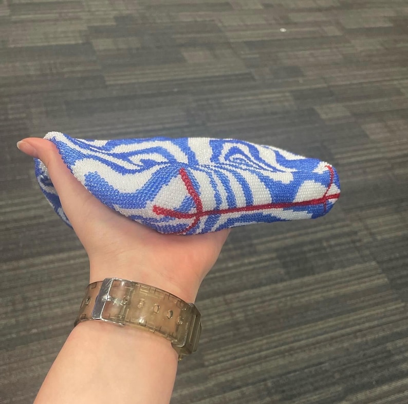 May include: A blue and white patterned fabric pouch with red stitching. The pouch is being held in a hand.