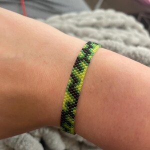 Peut inclure: Un bracelet en perles noir, vert et jaune avec un motif géométrique.