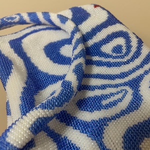 May include: A white and blue beaded bag with a swirling pattern. The bag has a single handle and is made of small, round beads.