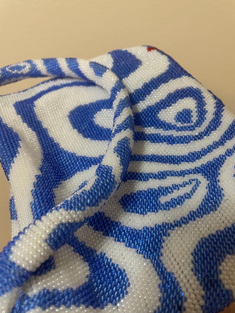 May include: A white and blue beaded bag with a swirling pattern. The bag has a single handle and is made of small, round beads.