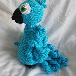 Puede incluir: Un p&aacute;jaro azul de crochet con un pico negro y un ojo blanco. El p&aacute;jaro tiene una cola larga y plumosa.
