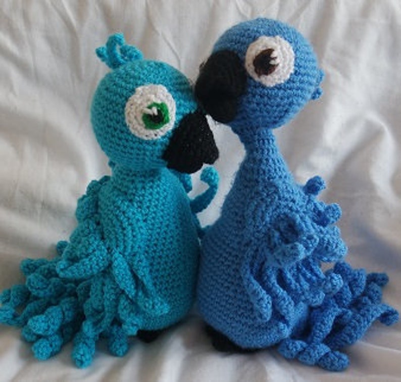 Puede incluir: Dos peluches de p&aacute;jaros azules de crochet con picos y ojos negros. El p&aacute;jaro de la izquierda tiene un ojo verde, y el p&aacute;jaro de la derecha tiene un ojo marr&oacute;n.