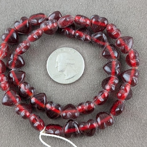 May include: A strand of red glass heart-shaped beads. The beads are translucent and have a slight shimmer. The beads are strung on a clear thread.