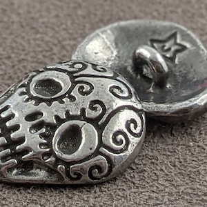 May include: Silver skull button with a decorative swirl pattern and a star on the back.