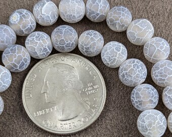 May include: A strand of white agate beads with a white and gray marbled pattern. The beads are round and smooth, and they are arranged in a circle around a US quarter.