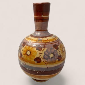 May include: A hand-painted ceramic vase with a round body and a long neck. The vase features a floral design in shades of brown, yellow, and purple, with horizontal stripes. The vase is a decorative item.