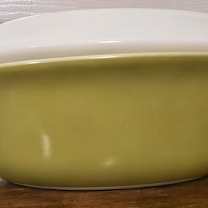 May include: A green oval-shaped casserole dish with a white lid. The dish is made of glass and has a smooth, glossy finish.