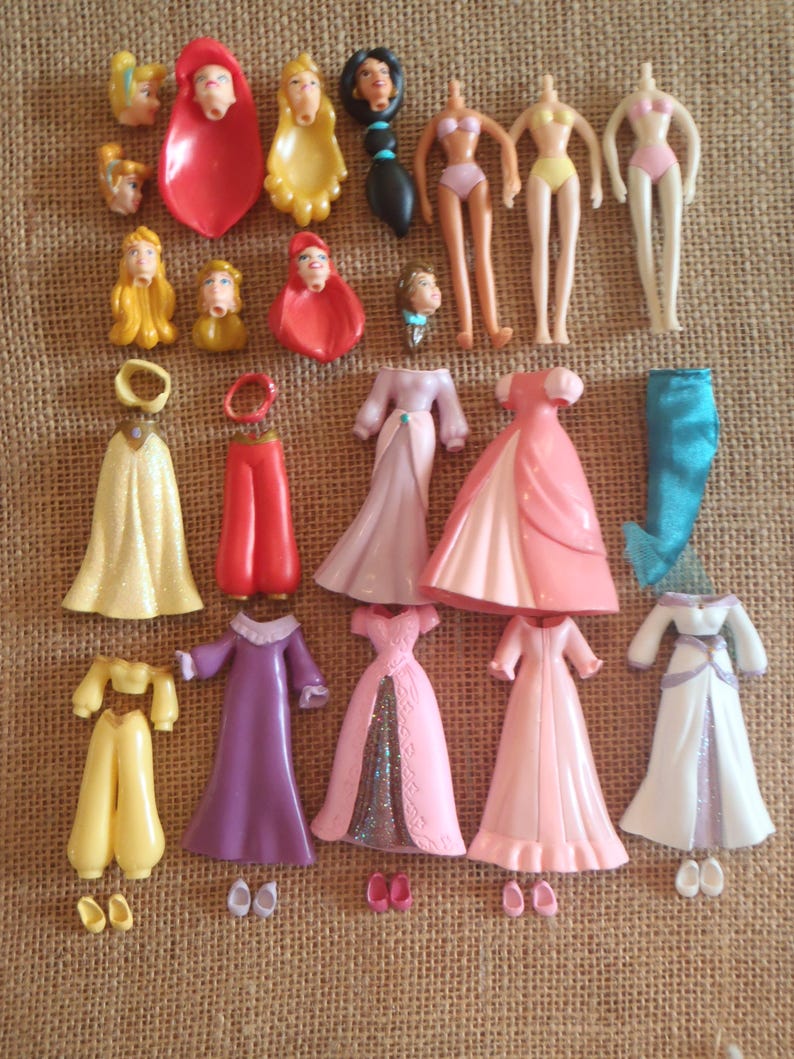 May include: A collection of vintage doll parts, including heads, torsos, and various outfits. The outfits include dresses in shades of pink, white, and purple, as well as pants and tops in yellow and red. The dolls are missing their heads.
