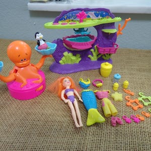 May include: A colorful vintage playset featuring an orange octopus with a pink base, a purple underwater-themed structure, a mermaid doll, and various accessories. Includes a penguin and a polar bear.