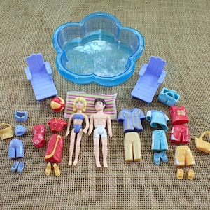 May include: A set of miniature beach toys, featuring two dolls, a pool, sun loungers, clothing, and accessories. The dolls are in swimwear. Accessories include a beach ball, shoes, and a basket. The pool is shaped like a flower.