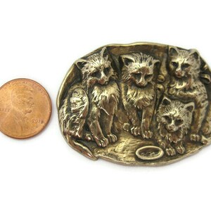 Peut inclure: Une broche en m&eacute;tal dor&eacute; repr&eacute;sentant quatre chatons dans une sc&egrave;ne ludique. Les chatons sont repr&eacute;sent&eacute;s en relief, en trois dimensions.