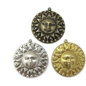 May include: Three metal sun charms with a face in the center. The sun charms are in gold, silver, and antique brass.