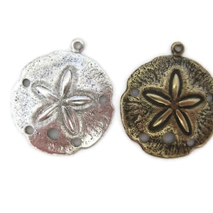 May include: Two sand dollar charms, one silver and one antique brass, with a five-pointed star design. Both charms have four holes around the edge.