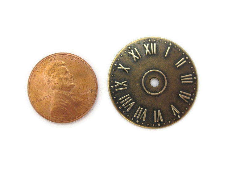 May include: A close-up of a brass clock face with Roman numerals. The clock face is about the size of a US penny.