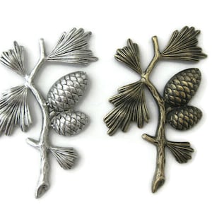 May include: Two silver and gold pine branch charms with pine cones. The charms are detailed and have a rustic look.