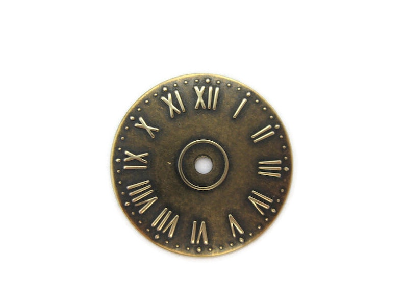 May include: A round, antique gold-toned clock face with Roman numeral markings. The clock face has a small hole in the center.
