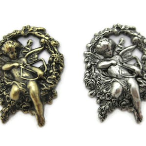 May include: Two metal charms featuring a cherub holding a bow and arrow, surrounded by a floral wreath. One charm is gold-toned, the other is silver-toned.