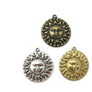 May include: Three sun charm pendants with a face in the center. The charms are gold, silver, and bronze.