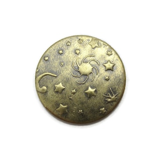 May include: A round, gold-colored metal charm with a design of a sun and stars. The charm has a textured surface and a slightly worn look.