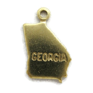 May include: Gold-colored metal charm shaped like the state of Georgia with the word "GEORGIA" inscribed on it.