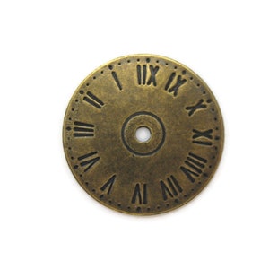 May include: A gold-toned metal clock face with Roman numeral markings. The clock face has a small hole in the center.