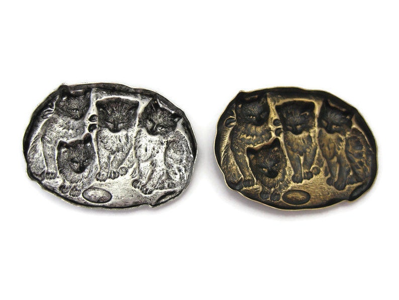 Peut inclure: Une broche ovale en argent et or avec un motif de quatre chatons jouant avec une balle. Les chatons sont en relief et la broche a une finition lisse et polie.