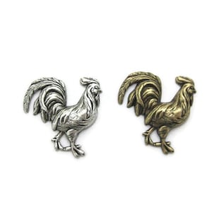 May include: Two metal rooster figurines. One is silver-colored, the other is gold-colored. Both have detailed feathers and stand in a walking pose. The roosters are on a white background.