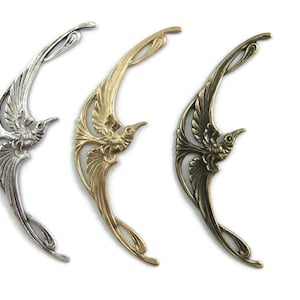 Könnte beinhalten: Drei metallene Vogel-Anhänger in Silber-, Gold- und Bronze-Finish. Jeder Anhänger zeigt einen stilisierten Vogel mit ausgebreiteten Flügeln und einem filigranen Design.