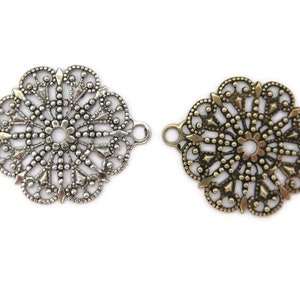 May include: Two ornate metal filigree connector charms, one silver and one gold, with a circular design and open loops on the sides.