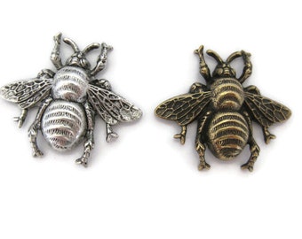May include: Two bee-shaped metal charms, one silver and one gold, with detailed wings and a textured body.