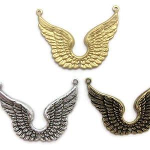 May include: Three metal wing charms in gold, silver, and bronze tones. Each charm features detailed feathering and a loop at the top for attaching to jewelry or other crafts. The wings are symmetrical and curved.