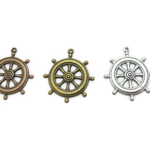 May include: Three metal ship wheel charms in different finishes: antique gold, gold, and silver. Each charm has a detailed design with spokes and a central hub.