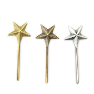 May include: Three star-shaped metal toppers in gold, brass, and silver. Each topper has a long, thin stem.