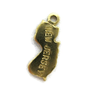 May include: Gold-colored metal charm shaped like the state of New Jersey with the words "NEW JERSEY" inscribed on the charm.