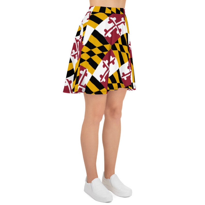 May include: A skater skirt featuring a bold geometric pattern in black, gold, white, and burgundy. The design includes a repeating pattern of a cross with a horizontal bar. The skirt is knee-length and made of a lightweight fabric.