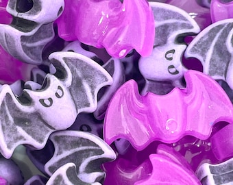 Op de afbeelding: Een close-up van een stapel paarse en zwarte plastic vleermuischarms. De vleermuizen hebben een glanzende, doorschijnende afwerking.
